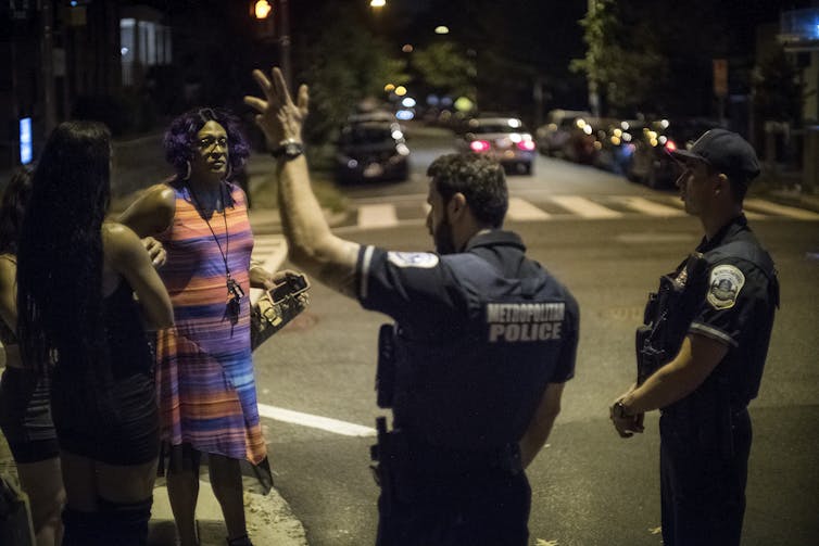 A woman talks with two police officers on a street at night