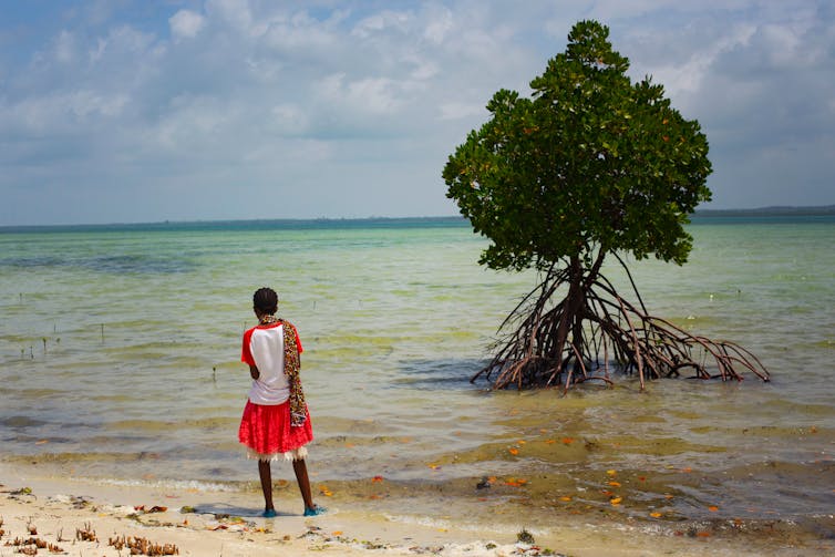 Girl looks into ocean beside a tree