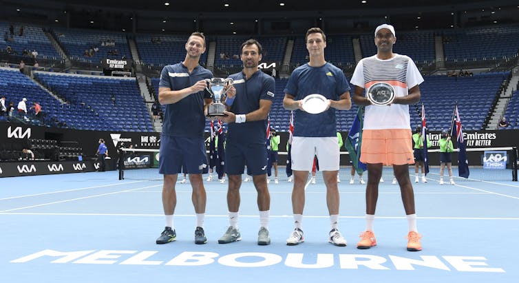 Four men stand on a tennis court at the Australian Open with vacant stadium seen in the background