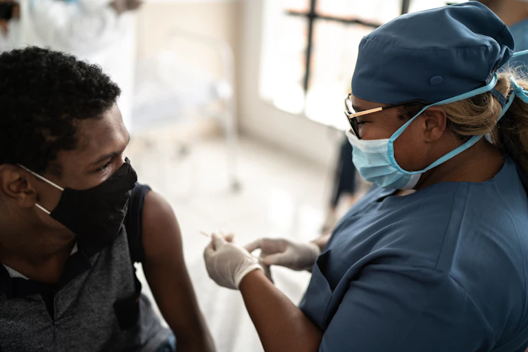 A teen receives a COVID-19 vaccine from a health care worker.