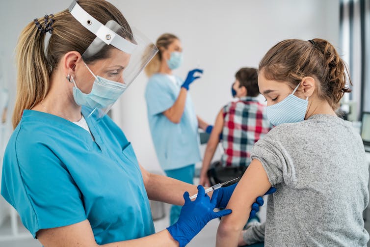 A health care worker injects a needle with the COVID-19 vaccine into the shoulder of a teen.