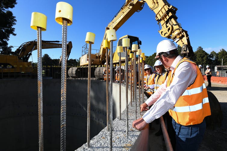 government ministers in high-viz vests and hard hats inspect work on construction project