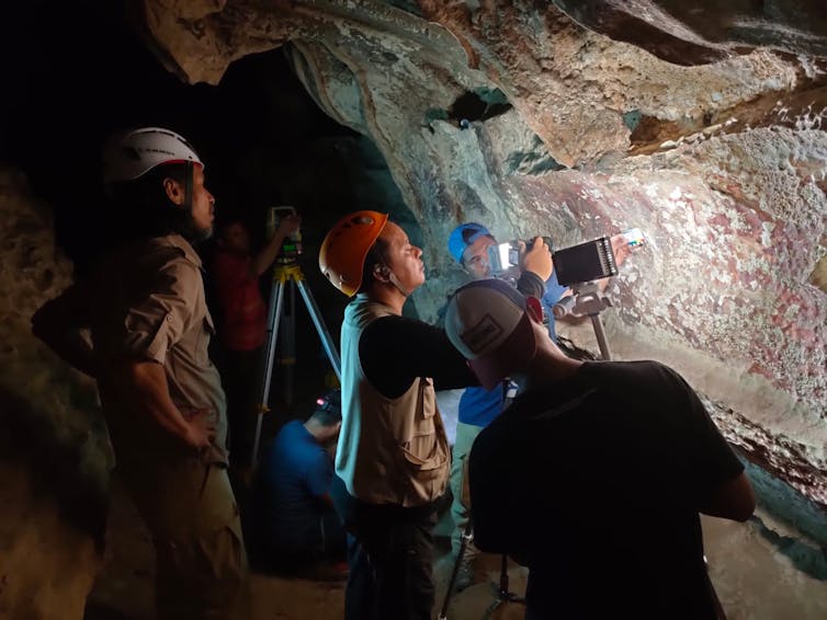 Three people hold a torch to cave wall