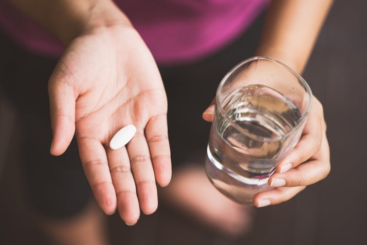 Person taking painkillers with glass of water