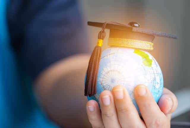 A hand holding globe with graduation hat on top.