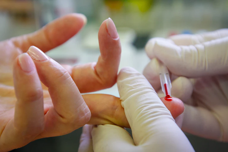 A person receives a finger prick blood test from a clinician.