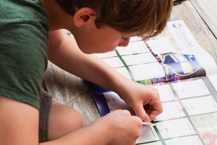A child putting a football sticker into an album.