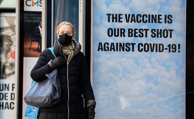 A woman walks past a sign saying that the vaccine is our best shot.
