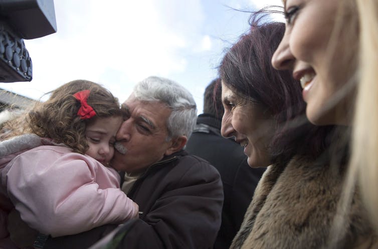 A Syrian-Canadian man hugs and kisses his newly arrived grand-daughter