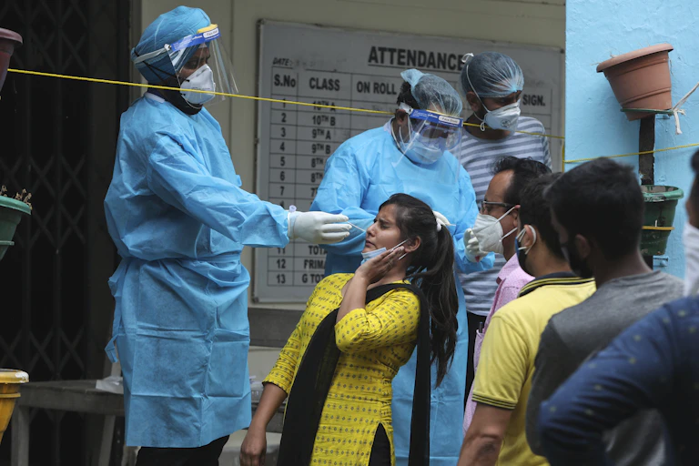 Indian woman leans back as health care worker swabs her nose for COVID-19 test, there is a line of people behind her