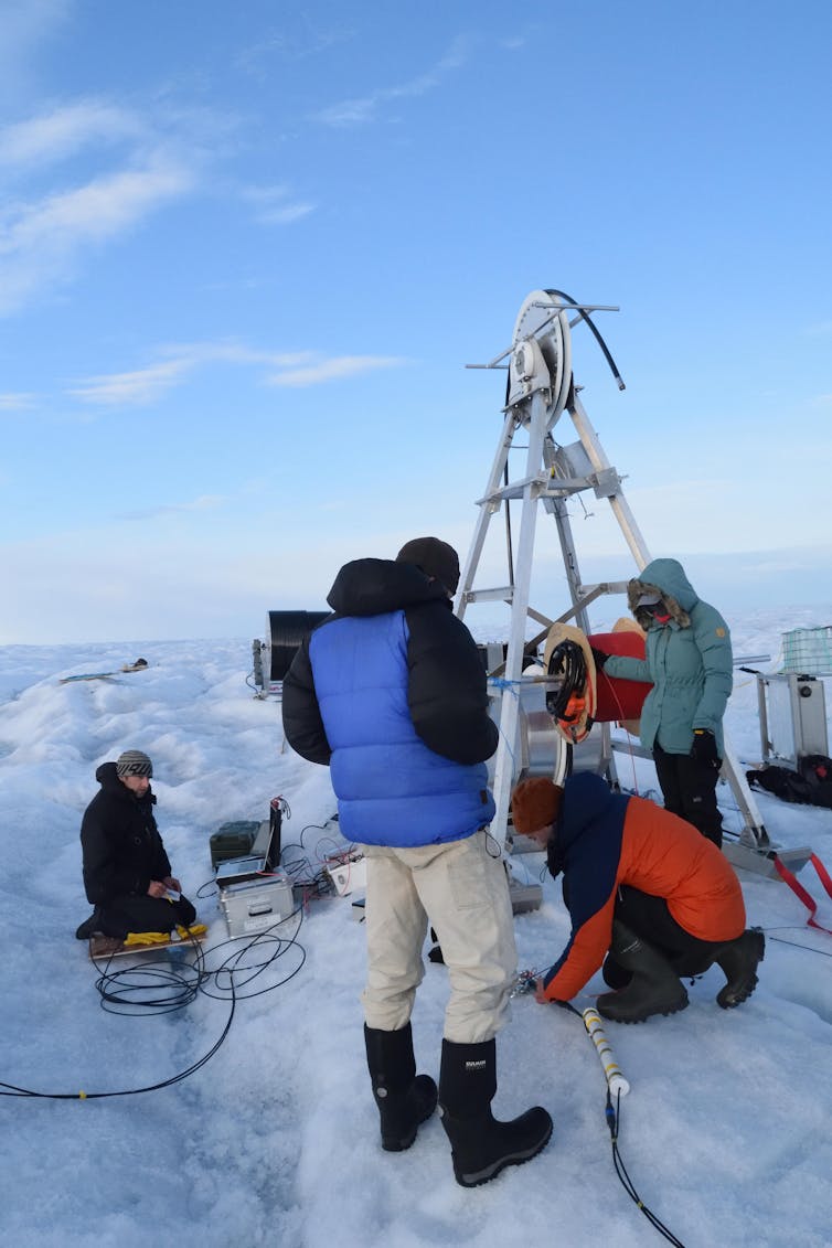 People stand around large equipment on an icy surface