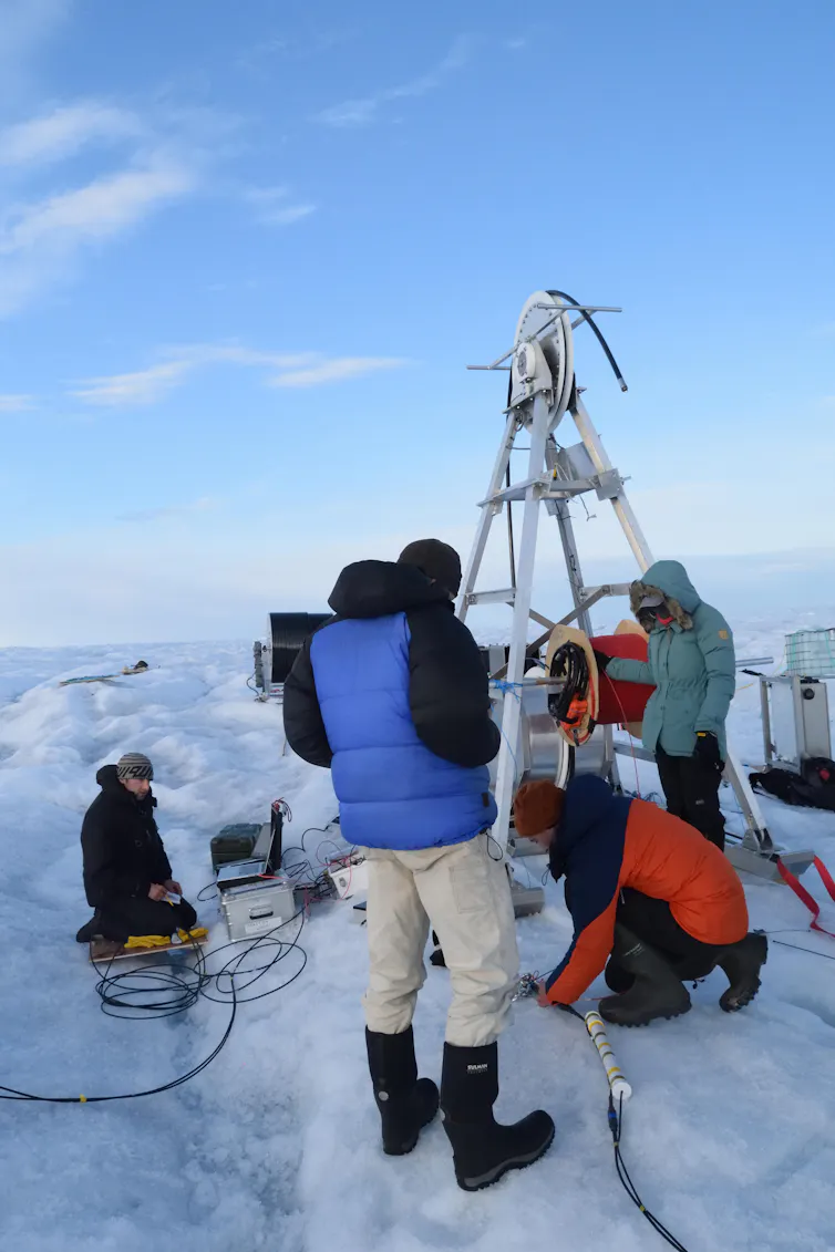 People stand around large equipment on an icy surface