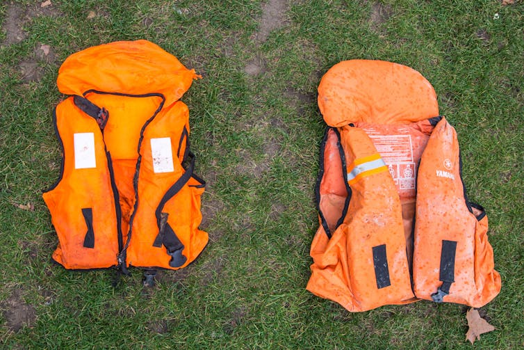 Two orange life jackets lie on the ground