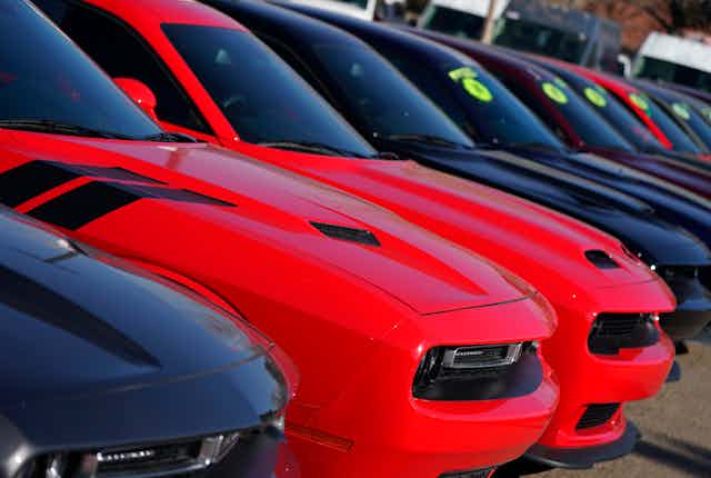 A row of used Dodge Challengers, red and black, sit in a dealership parking lot in Littleton, Colorado