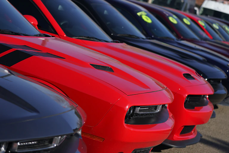 A row of used Dodge Challengers, red and black, sit in a dealership parking lot in Littleton, Colorado