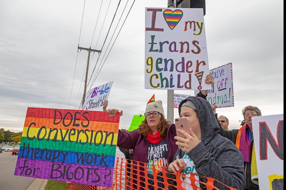 Protesters opposed to conversion therapy hold up protest signs that say 'I love my transgender child' and 'does conversion therapy work for bigots?'