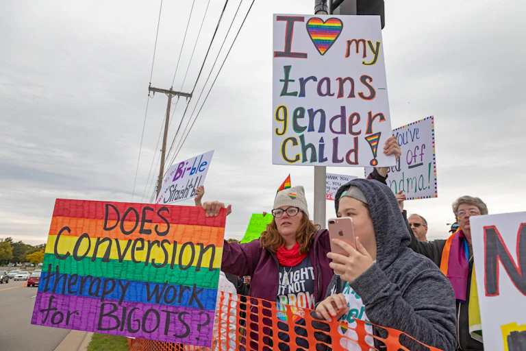 Protesters opposed to conversion therapy hold up protest signs that say 'I love my transgender child' and 'does conversion therapy work for bigots?'