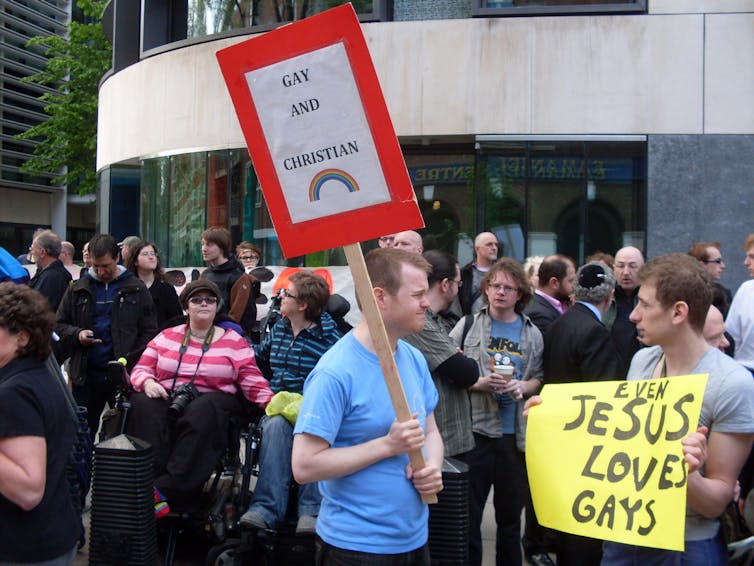 Protesters opposed to gay conversion therapy hold up signs saying 'gay and Christian' and 'Jesus loves gays'