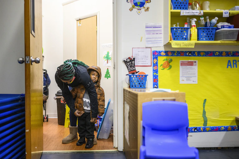 Child care worker zips up child's coat