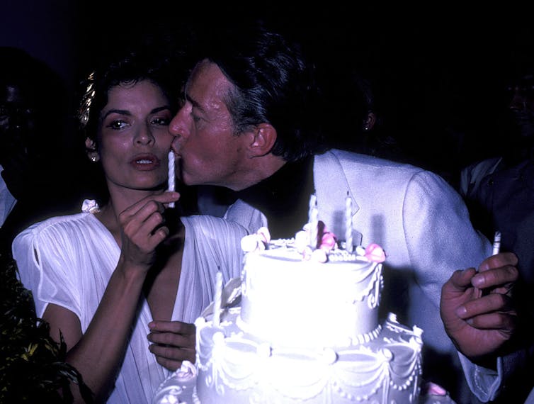 Halston kisses Bianca Jagger on the cheek behind her birthday cake.