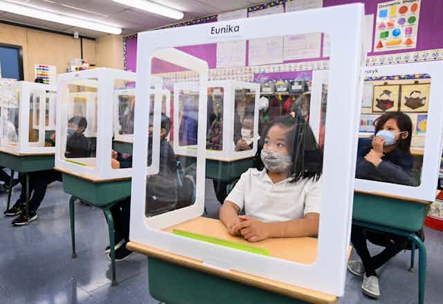 Masked children behind protective screens in a classroom