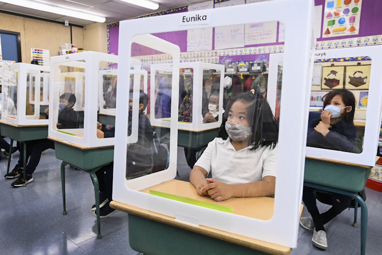 Masked children behind protective screens in a classroom