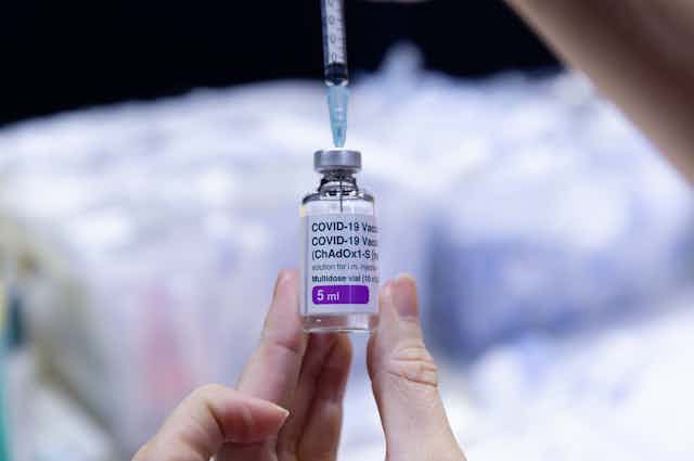 A hand holding a vial of AstraZeneca vaccine.