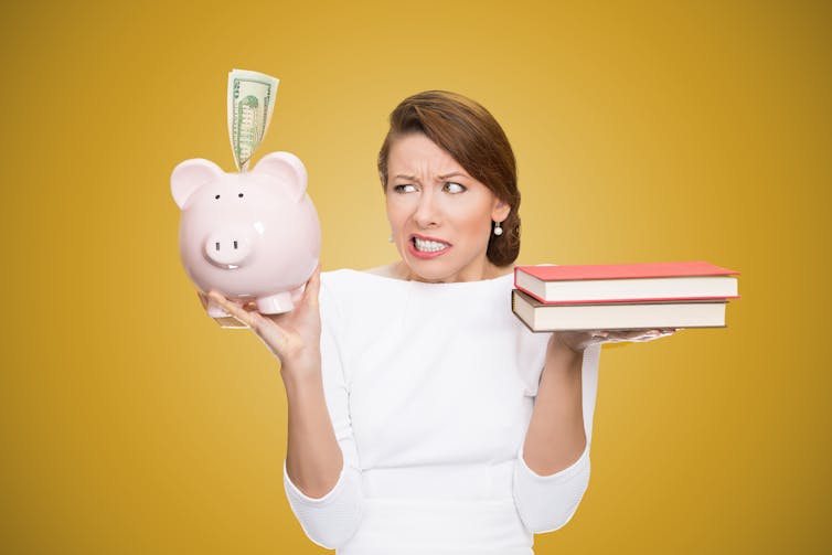 women weighs up books in one hand against piggybank in the other