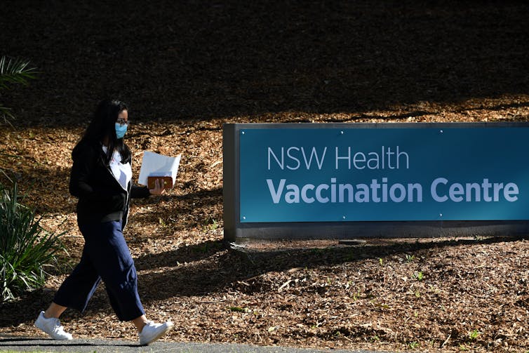 A woman walks past a sign which says 'NSW Health Vaccination Centre'.