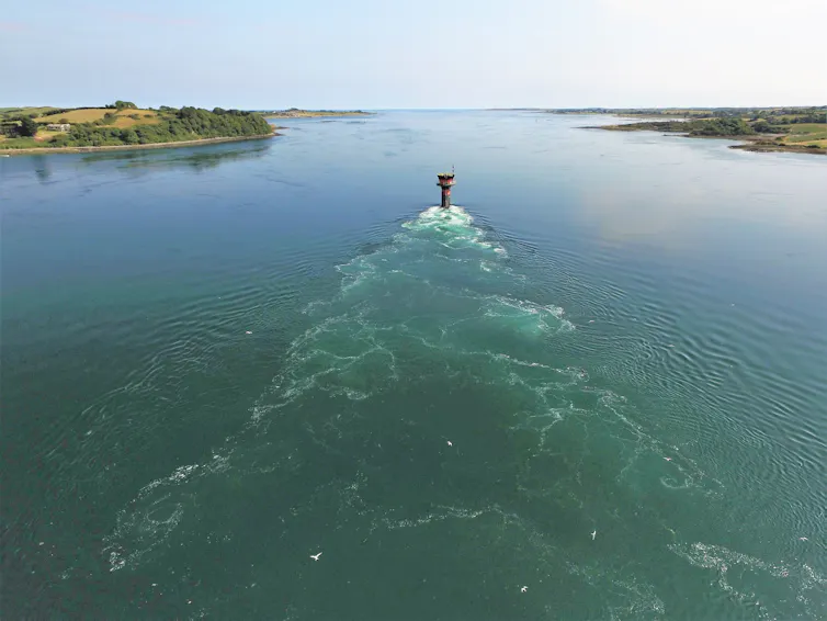 An aerial view of the sea, with turbulence caused by a human-made structure.