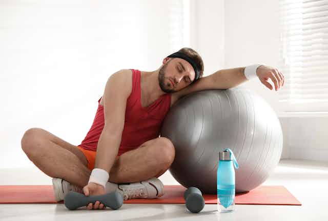 Homme en habit de sport dormant sur un gros ballon d'exercice