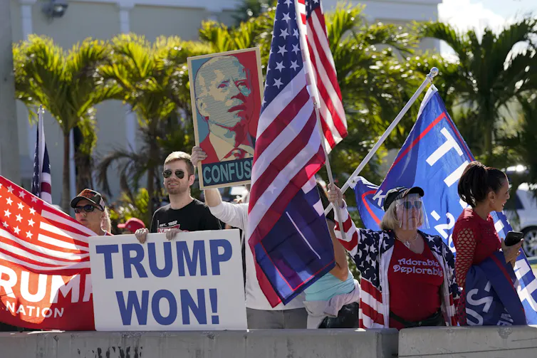 Trump supporters wave flags and hold a sign that say Trump Won