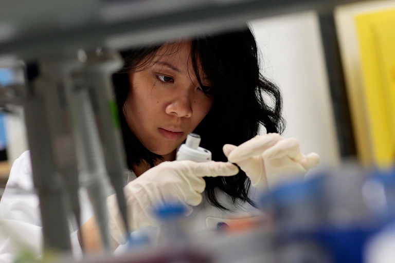 A woman wearing a white coat and gloves in a lab.