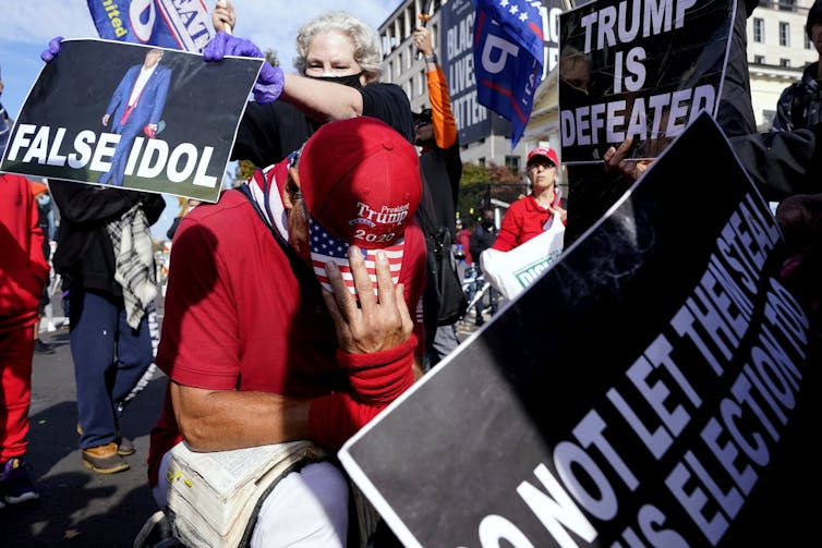 Um apoiador de Trump se ajoelha com uma Bíblia no Black Lives Matter Plaza cercado por apoiadores de Biden