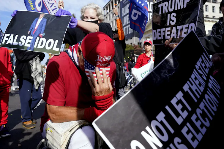 A Trump supporter kneels with a Bible in Black Lives Matter Plaza surrounded by Biden supporters