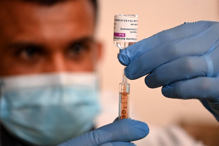 A health worker wearing a mask fills a syringe with COVID-19 vaccine.