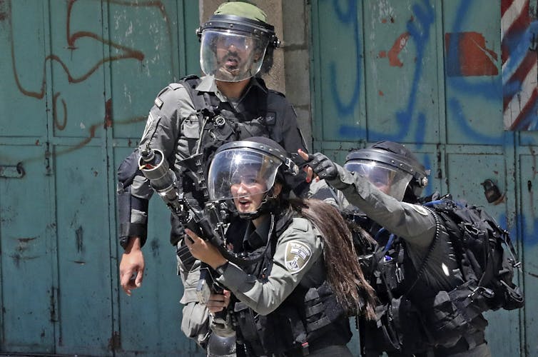 Three members of the Israeli security forces. One is firing tear gas.