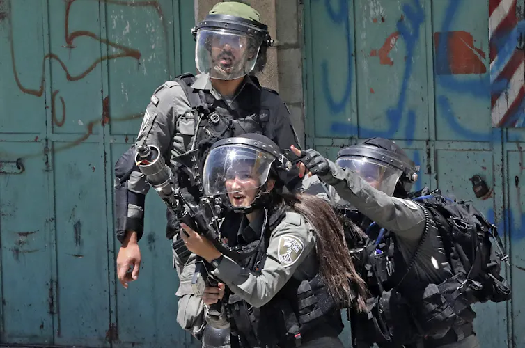 Three members of the Israeli security forces. One is firing tear gas.