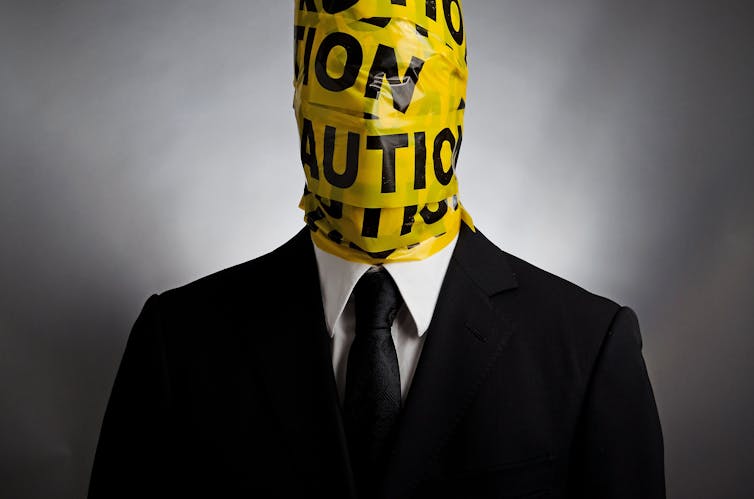Man in a suit and tie with yellow police tape wrapped around his head and neck.