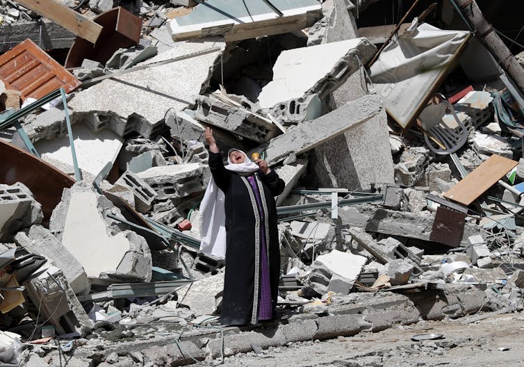 A woman cries standing near the rubble of a building.
