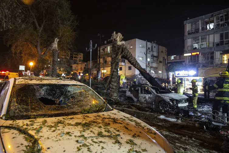 Rocket destruction, including decimated palm trees and cars covered in rubble and debris.