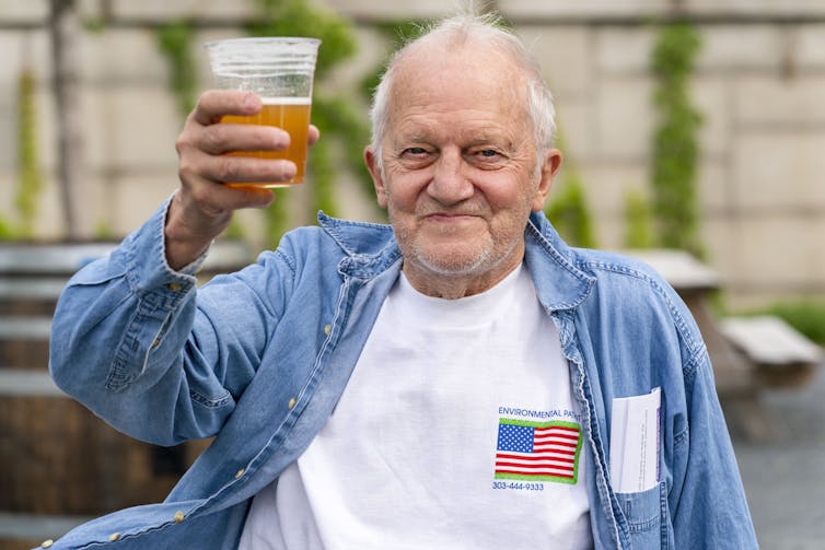 A man who just received a COVID-19 vaccine smiles as he holds up a cup with beer