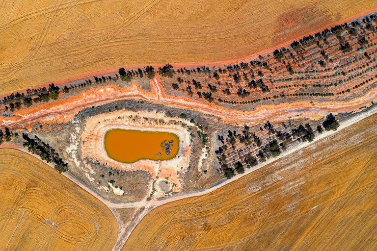 Aerial view of a drying dam, surrounded by wheat fields,