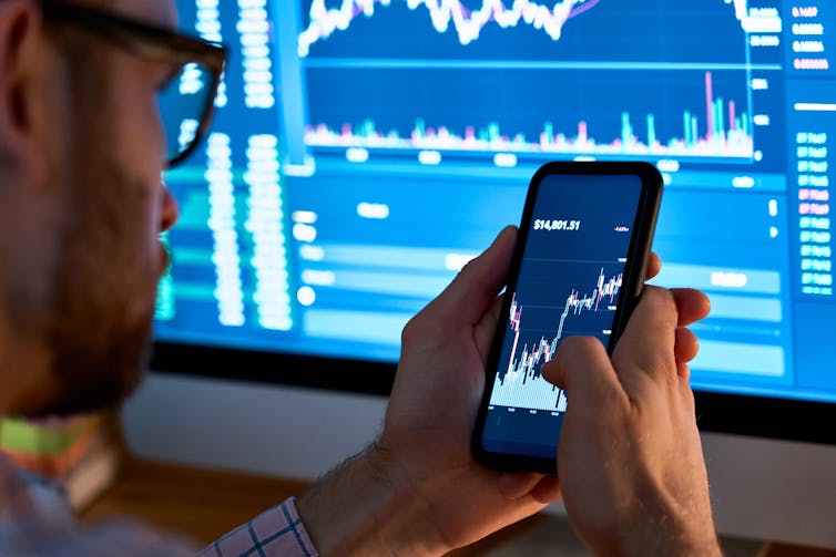 Man holds smartphone in front of computer screen