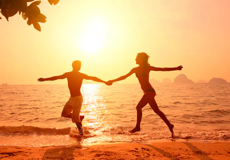 A couple running together on a beach at sunset