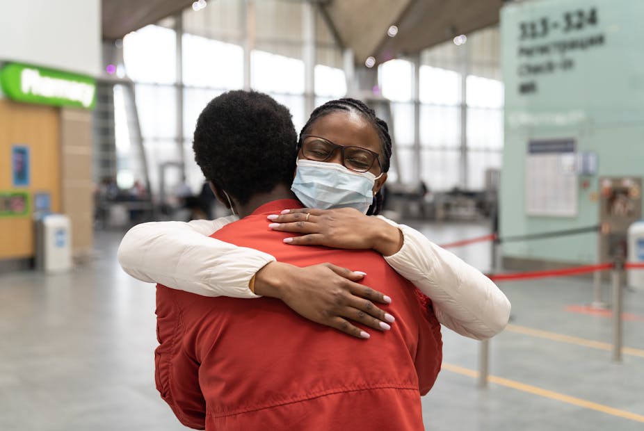 A woman wearing a face mask hugs a man in the airport.