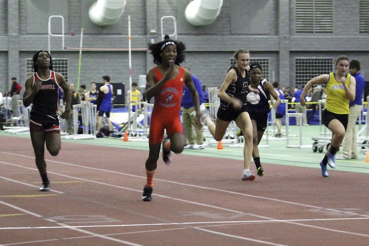 Four sprinters run at an indoor track meet.