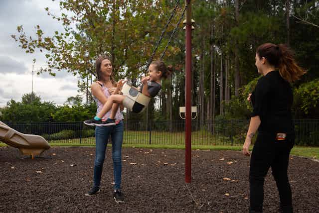 Trans mom and her wife push their child on a swing 