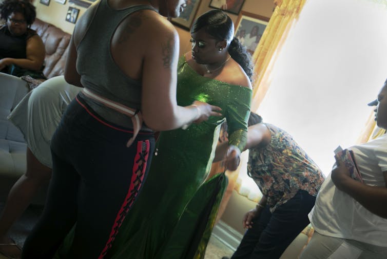 A young girl wearing an emerald dress prepares for prom with her family.