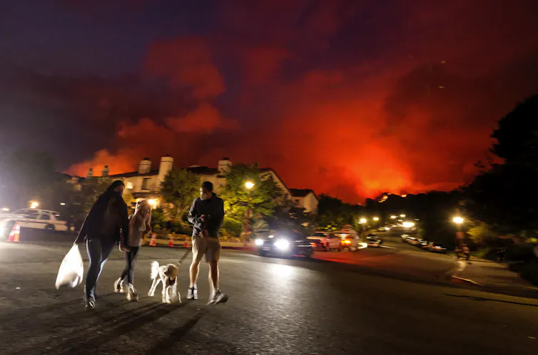 People evacuate their homes at night as a wildfire burns nearby